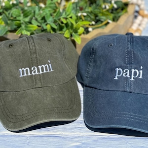 May include: Two baseball caps, one green with the word "mami" embroidered in white, and one blue with the word "papi" embroidered in white.