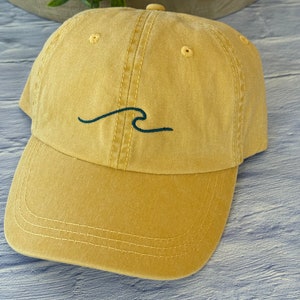 May include: A mustard yellow baseball cap with a black embroidered wave design.