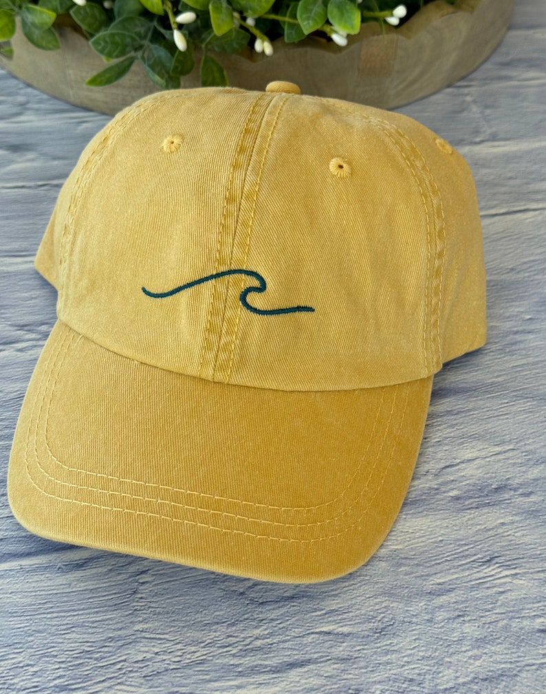 May include: A mustard yellow baseball cap with a black embroidered wave design.
