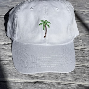 May include: White cotton baseball cap with an embroidered green palm tree on the front.