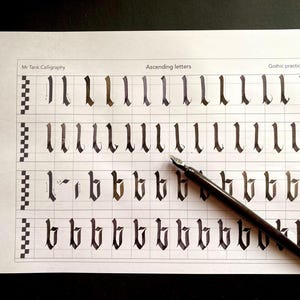 Op de afbeelding: Een oefenblad voor gotische kalligrafie met een rasterpatroon en meerdere rijen van de letter "l" en "b" geschreven in zwarte inkt. Een zwarte kalligrafiepen ligt op het blad.