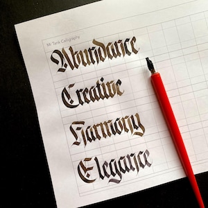 Op de afbeelding: Een wit vel papier met een rasterpatroon en vier woorden in zwarte inkt geschreven: Overvloed, Creatief, Harmonie en Elegantie. Een rode kalligrafiepen ligt op het papier.