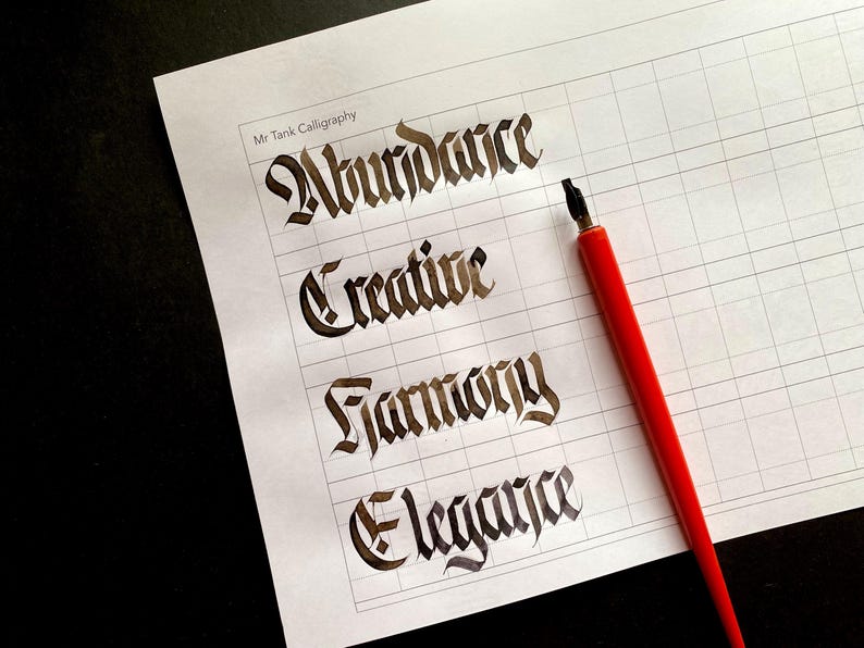 Op de afbeelding: Een wit vel papier met een rasterpatroon en vier woorden in zwarte inkt geschreven: Overvloed, Creatief, Harmonie en Elegantie. Een rode kalligrafiepen ligt op het papier.