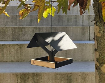 May include: A black metal bird feeder with a wooden tray. The feeder has a roof and a tree-like design. The feeder is hanging from a tree branch.
