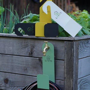 May include: A collection of garden accessories, including a green hose holder with a brass faucet, and various colored hanging tags. The tags are in white, yellow, and black, each with the "LIVIO" logo. The scene is set against a wooden background.