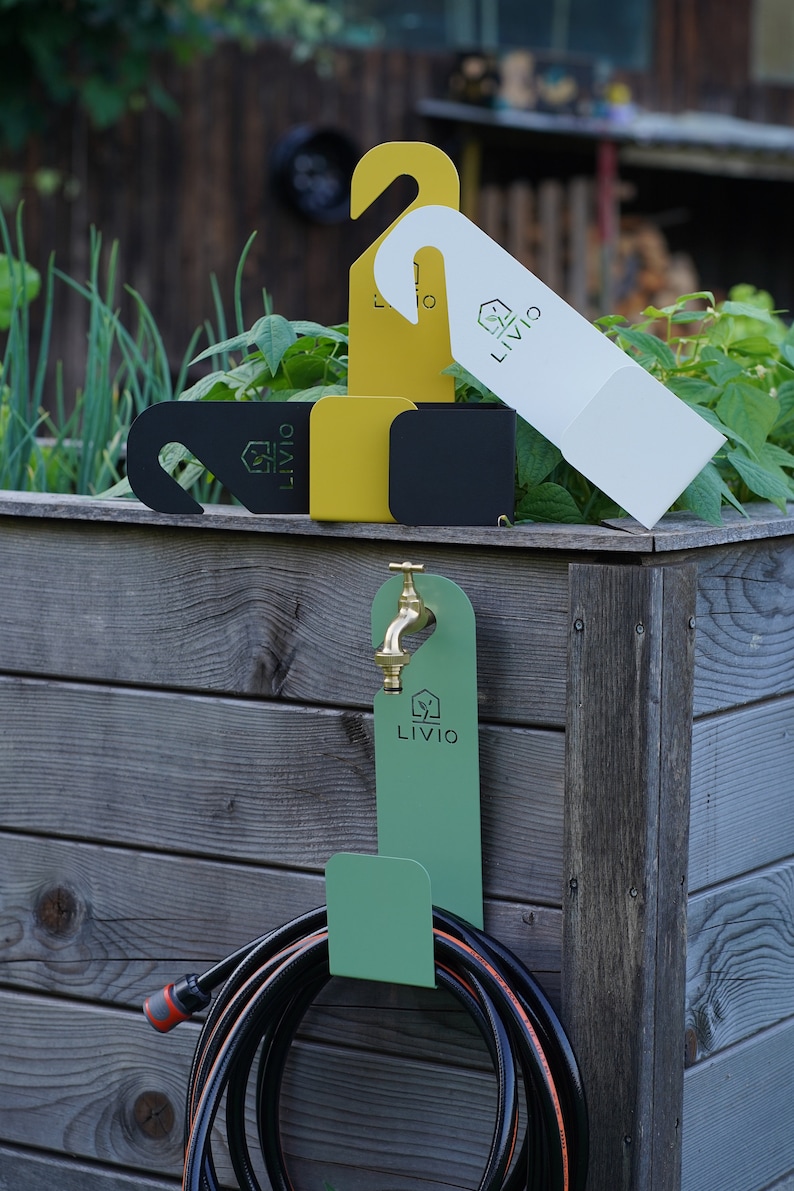 May include: A collection of garden accessories, including a green hose holder with a brass faucet, and various colored hanging tags. The tags are in white, yellow, and black, each with the "LIVIO" logo. The scene is set against a wooden background.