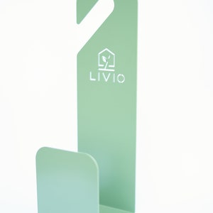 May include: A mint green metal hook with a curved base and a top hook for hanging. The word "LIVIO" is printed in white, along with a house and leaf logo. The hook is designed for organizing items.