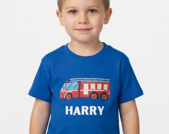 May include: A royal blue short-sleeved t-shirt featuring a graphic of a red fire truck with a silver ladder on top. Below the fire truck, the name HARRY is printed in bold, white, uppercase letters centered on the chest of the garment.