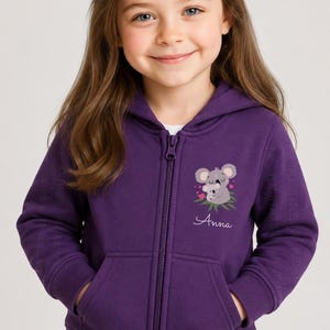 May include: A deep purple zip-up hooded sweatshirt featuring a graphic of a koala holding a baby koala on the left chest. The graphic includes small pink hearts and green leaves. The name Anna is printed in white cursive script below the koala graphic.