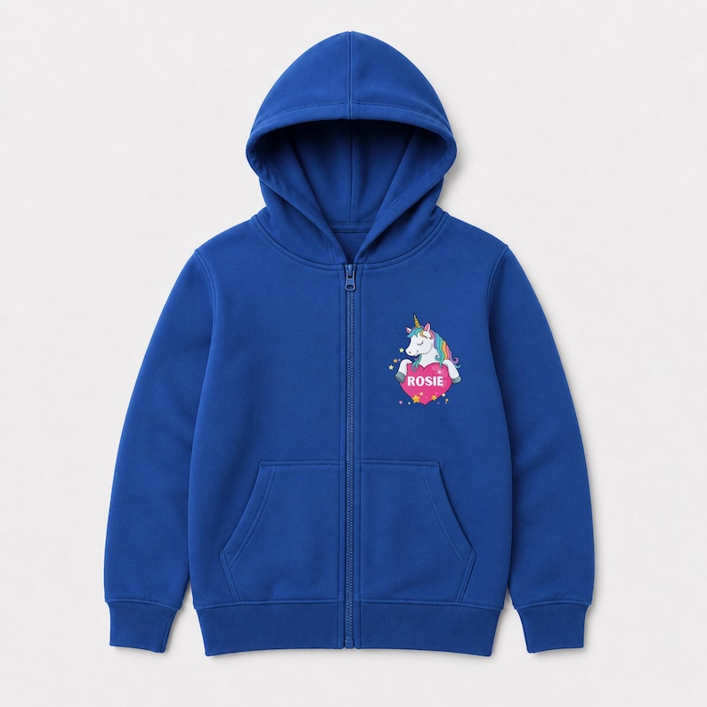May include: A royal blue zip-up hoodie featuring a hood, long sleeves, and two front pockets. On the left chest, there is a graphic of a white unicorn with a rainbow mane and a gold horn, resting on a pink heart that displays the name ROSIE.