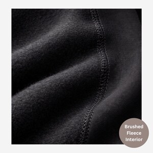 May include: A black fabric garment featuring a soft brushed fleece interior texture. The material displays a visible vertical seam with reinforced stitching connecting the fuzzy fleece side to a smoother, ribbed-knit fabric section on the right.