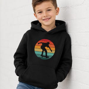May include: A black hooded sweatshirt featuring a circular graphic on the chest. The graphic displays a silhouette of a person skateboarding against a background of horizontal stripes in shades of red, orange, yellow, and teal, creating a retro effect.