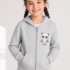May include: A light gray zip-up hoodie featuring a cute panda bear graphic with a floral crown. The panda has black and white details and the name "Elisa" is printed below. The hoodie has a full zipper and two front pockets.