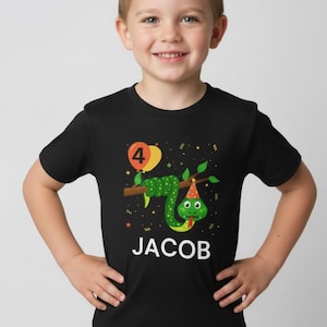 May include: Black t-shirt with a cartoon snake wearing a party hat and holding a balloon with the number 4. The name "JACOB" is printed in white below the snake. The shirt is designed for a child's birthday.