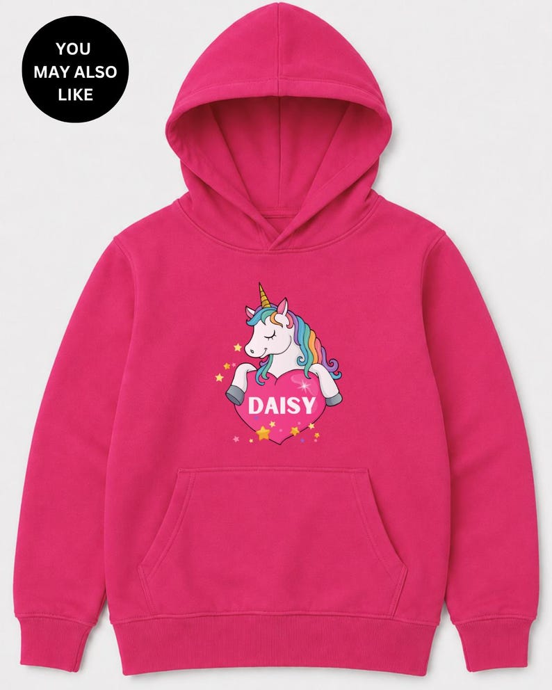 May include: A bright fuchsia long-sleeve hooded sweatshirt featuring a central graphic of a white unicorn with a rainbow mane and a gold horn. The unicorn rests on a large pink heart containing the white text DAISY, surrounded by small yellow stars.