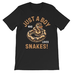 Peut inclure: T-shirt noir avec un motif de serpent enroulé dans des tons marron et beige. Le texte "JUST A BOY WHO LOVES SNAKES!" est imprimé en marron. Le t-shirt est fabriqué dans un matériau doux, idéal pour un usage quotidien.