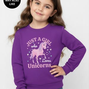 May include: A purple long-sleeve sweatshirt featuring a graphic print of a pink unicorn surrounded by small stars and hearts. The text printed on the front reads, "JUST A GIRL who Loves Unicorns" in light pink lettering with a white outline.