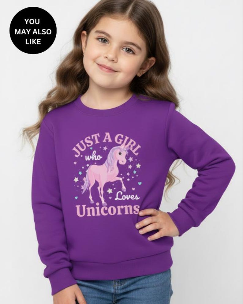 May include: A purple long-sleeve sweatshirt featuring a graphic print of a pink unicorn surrounded by small stars and hearts. The text printed on the front reads, "JUST A GIRL who Loves Unicorns" in light pink lettering with a white outline.