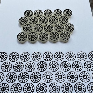 Puede incluir: Un sello de goma blanco con un patrón repetitivo de círculos negros con un círculo más pequeño en el interior. El sello se utiliza para crear un borde del mismo patrón en una hoja de papel blanca.