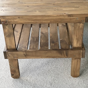 May include: A rustic wooden end table with a single shelf. The table is made of brown stained wood and has a simple design.
