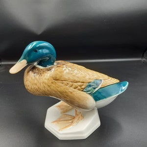 May include: A ceramic duck figurine with a teal head, tan body, and white base. The duck has a detailed design with realistic feather textures and a light-colored beak. The figurine is a decorative item.