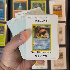 Pu&ograve; includere: Un mucchio di carte collezionabili Pok&eacute;mon, con una carta Kabuto della serie Neo Discovery. La carta mostra il nome "Kabuto" e "50 HP". Il numero del set &egrave; 56/75.