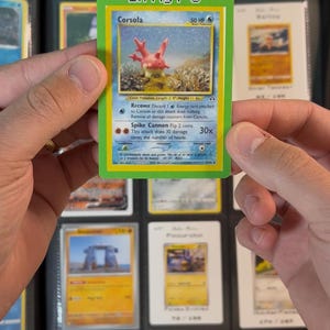 Pu&ograve; includere: Una carta Pok&eacute;mon Corsola con bordo verde con la scritta "In My PC" in alto. La carta presenta una creatura simile al corallo con uno sfondo blu e varie descrizioni di attacco. La carta &egrave; tenuta in un raccoglitore.