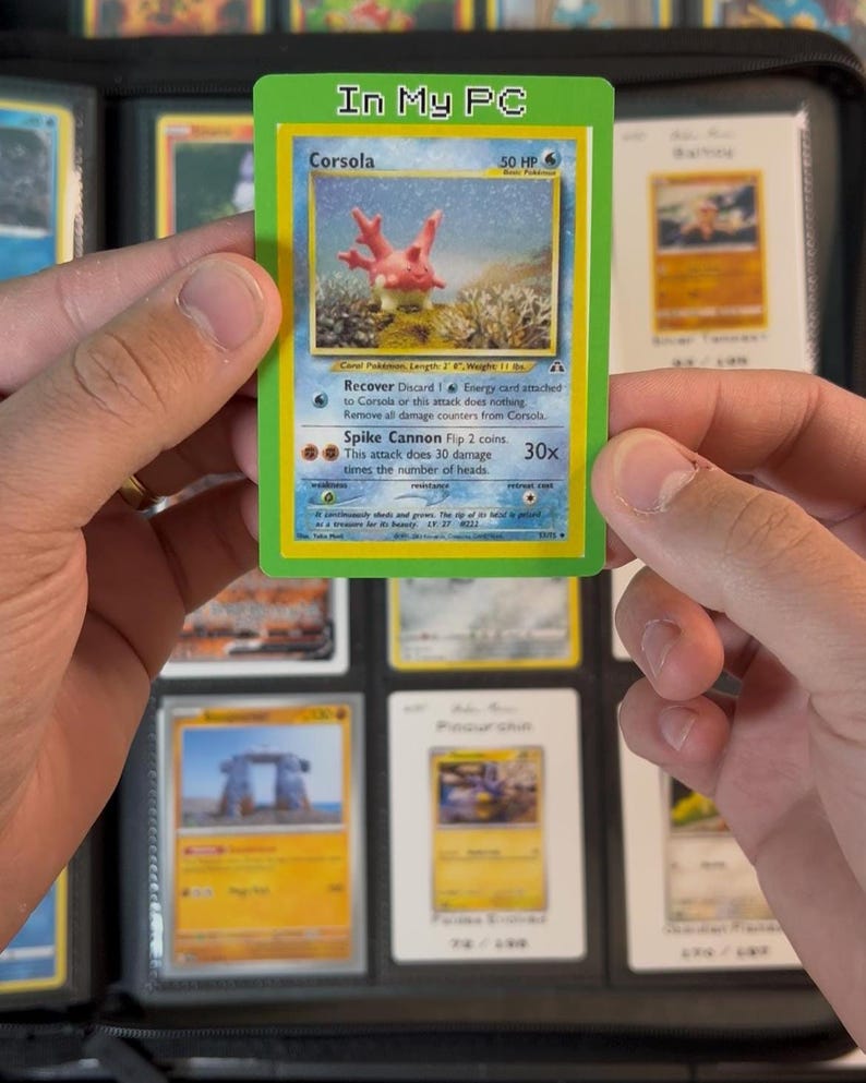 Pu&ograve; includere: Una carta Pok&eacute;mon Corsola con bordo verde con la scritta "In My PC" in alto. La carta presenta una creatura simile al corallo con uno sfondo blu e varie descrizioni di attacco. La carta &egrave; tenuta in un raccoglitore.