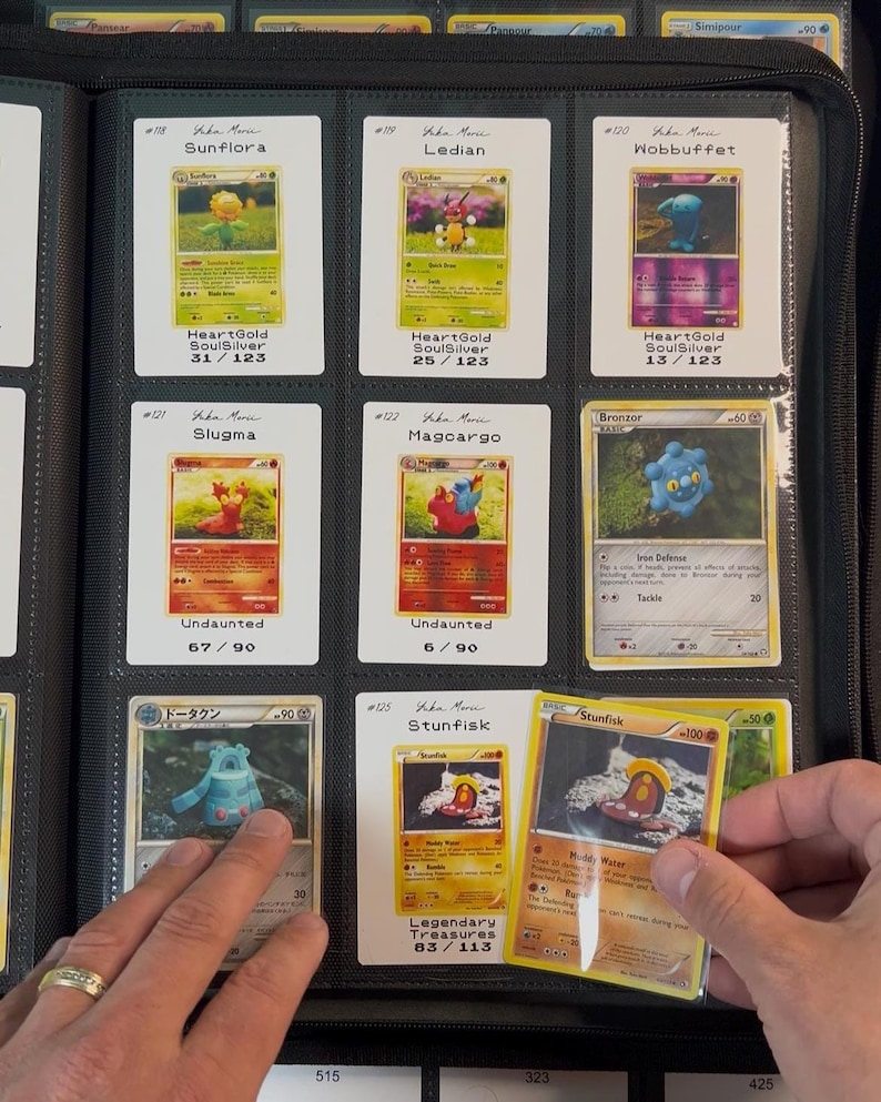 Pu&ograve; includere: Una collezione di carte collezionabili Pok&eacute;mon esposta in un raccoglitore nero. Le carte presentano vari personaggi come Sunflora, Ledian e Stunfisk, con testo che indica nomi di set e numeri di carte. Il raccoglitore &egrave; aperto e una mano tiene in mano una carta.