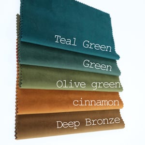 May include: A stack of five rectangular fabric swatches with pinked edges, featuring a soft velvet texture. The colors from top to bottom are labeled as Teal Green, Green, Olive green, cinnamon, and Deep Bronze in white text on each piece.