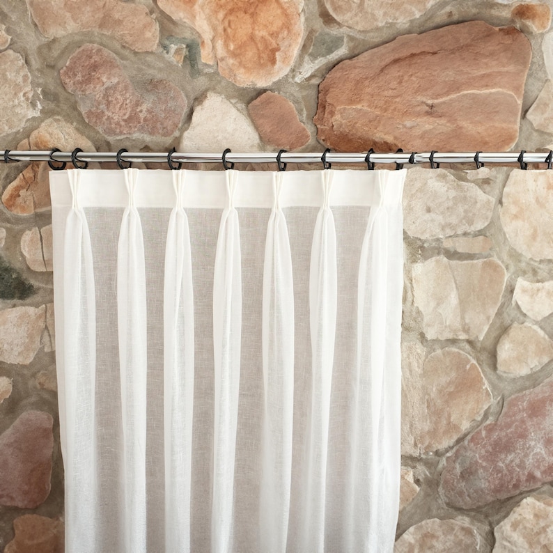 Pode incluir: Cortinas brancas e transparentes penduradas em uma haste de cortina de metal contra um fundo de parede de pedra.
