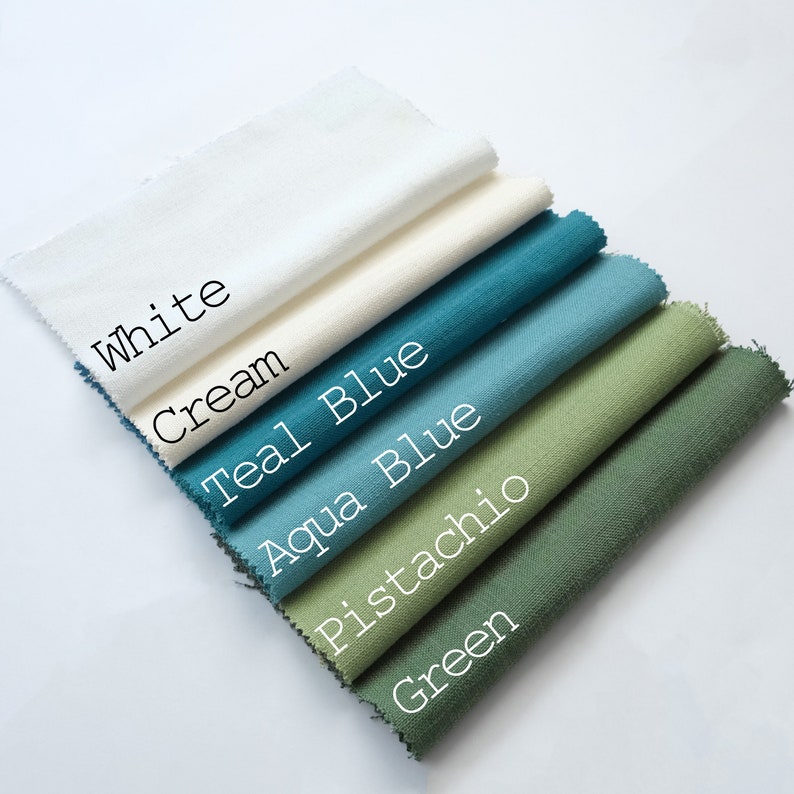 Pu&ograve; includere: Una pila di sei campioni di tessuto rettangolari con bordi sfilacciati, disposti in un motivo diagonale a cascata. I colori sono etichettati come White, Cream, Teal Blue, Aqua Blue, Pistachio e Green, ognuno con una trama tessuta visibile.