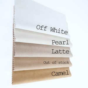 May include: A stack of five fabric swatches with pinked edges, arranged in a gradient from light to dark. The labels printed on the fabric are Off White, Pearl, Latte, Out of stock, and Camel, representing the color options for the material.