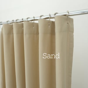 Pu&ograve; includere: Una tenda da doccia color sabbia tinta unita appesa a un'asta in cromo lucido con anelli in metallo argentato. Il tessuto presenta una trama visibile e pieghe verticali. La parola Sand &egrave; stampata in bianco sulla parte anteriore della tenda.