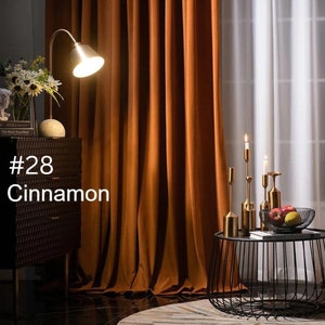 May include: Floor-to-ceiling cinnamon-colored curtains with vertical folds, positioned next to a black textured cabinet with a lamp and a black wire side table holding gold candle holders and a bowl of fruit. The text #28 Cinnamon is visible.