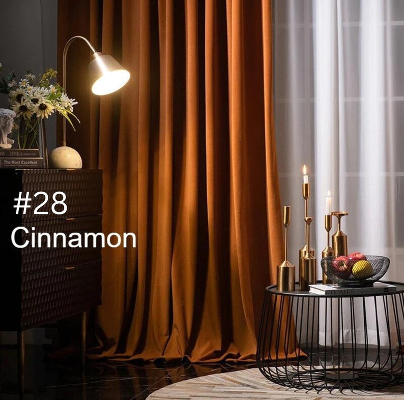 May include: Floor-to-ceiling cinnamon-colored curtains with vertical folds, positioned next to a black textured cabinet with a lamp and a black wire side table holding gold candle holders and a bowl of fruit. The text #28 Cinnamon is visible.