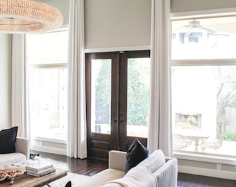 May include: A living room with a large white sofa, white curtains, and a wooden coffee table. The room has a large window and a set of French doors leading to the garden.