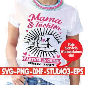 May include: White t-shirt with pink text that reads "Mama & Tochter" and a black and white illustration of two hands clasped together. The text "Partner in Crime Since 2017" is also on the shirt.