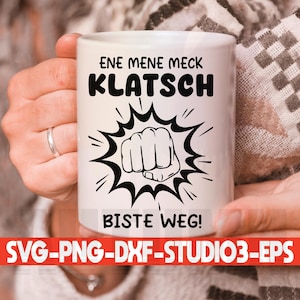 Könnte beinhalten: Weiße Keramiktasse mit schwarzem Text und einer schwarzen Faustgrafik. Der Text lautet "Ene mene meck Klatsch Biste weg!"