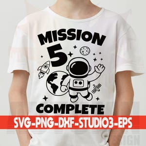 Może przedstawiać: Biała koszulka z czarną grafiką przedstawiającą astronautę, rakietę, planetę Ziemię i napis "MISSION 5 COMPLETE". Gwiazdy, księżyc i satelita dopełniają projekt.