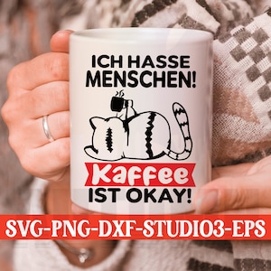 Puede incluir: Taza de cerámica blanca con una ilustración en blanco y negro de un gato sosteniendo una taza de café. El texto en la taza dice "Ich hasse Menschen! Kaffee ist okay!"