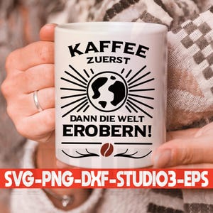 以下が含まれることがあります： 黒い文字で「Kaffee zuerst dann die Welt erobern!」と書かれた白いセラミックマグカップ。テキストは黒いサンバーストデザインで囲まれています。マグカップの底にはコーヒー豆があります。