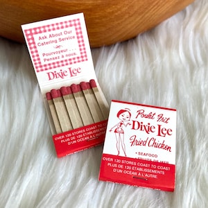 May include: Two vintage Dixie Lee matchbooks. One is open, showing red-tipped matches. The other matchbook features a cartoon woman and the text "Poulet Frit Dixie Lee Fried Chicken". Both matchbooks have red and white designs.