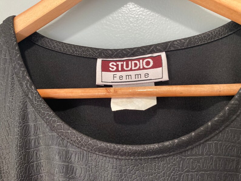 Puede incluir: Camiseta negra con un patr&oacute;n texturizado similar al de cocodrilo. La camiseta tiene un escote redondo y una etiqueta que dice "Studio Femme".