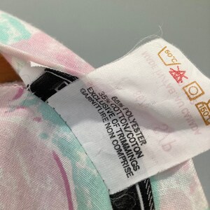 May include: White fabric care label with black text. The label states "65% Polyester 35% Cotton/Coton Exclusive of Trimmings Garniture Non Comprise". The label also has a care symbol for machine washing at 60 degrees Celsius and a symbol for tumble drying at a low temperature.