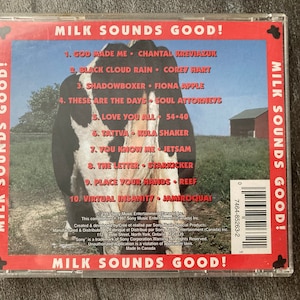 K&ouml;nnte beinhalten: Ein CD-Geh&auml;use mit rotem, wei&szlig;em und blauem Hintergrund, auf dem eine Kuh und ein roter Stall zu sehen sind. Der Titel der CD lautet "Milk Sounds Good!" und die Tracklist enth&auml;lt K&uuml;nstler wie Chantal Kreviazuk, Corey Hart, Fiona Apple und Soul Attorneys.