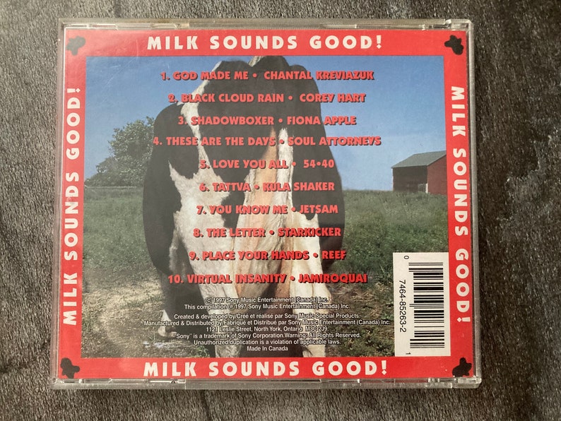 K&ouml;nnte beinhalten: Ein CD-Geh&auml;use mit rotem, wei&szlig;em und blauem Hintergrund, auf dem eine Kuh und ein roter Stall zu sehen sind. Der Titel der CD lautet "Milk Sounds Good!" und die Tracklist enth&auml;lt K&uuml;nstler wie Chantal Kreviazuk, Corey Hart, Fiona Apple und Soul Attorneys.