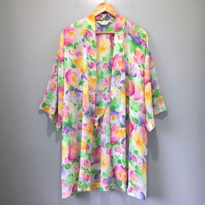 May include: A white silk robe with a floral print in shades of pink, yellow, green, and purple. The robe has a tie closure at the waist and short sleeves.