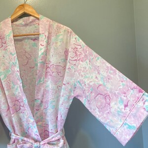 May include: A pink and white floral print robe with a long sleeve and a tie belt.