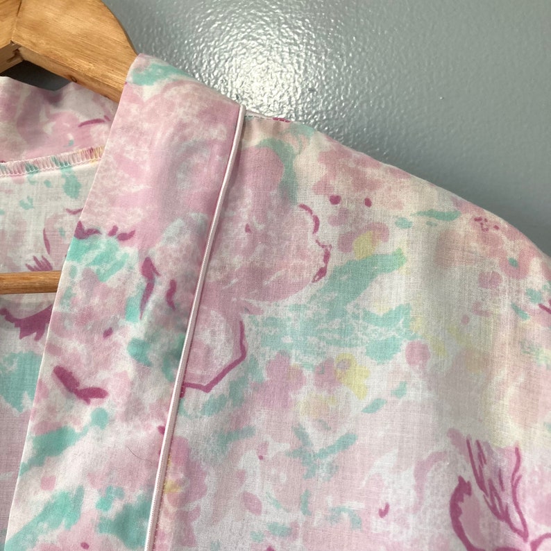 May include: A pink and white floral print dressing gown with a white trim around the collar and sleeves.